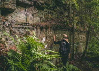 Kvinna som står vid en bergsvägg med handen på berget.