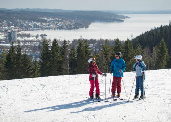 Three children in colorful clothes with skis on top of Ulricehamn Ski Center.