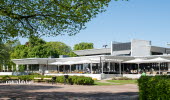 A hotel and their outdoor terrace, in front of is a large gravel field.