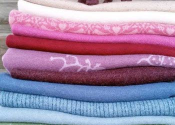 En bild på vikta tyger av ull som lagts i en hög. På toppen står en häst av tovad ull.