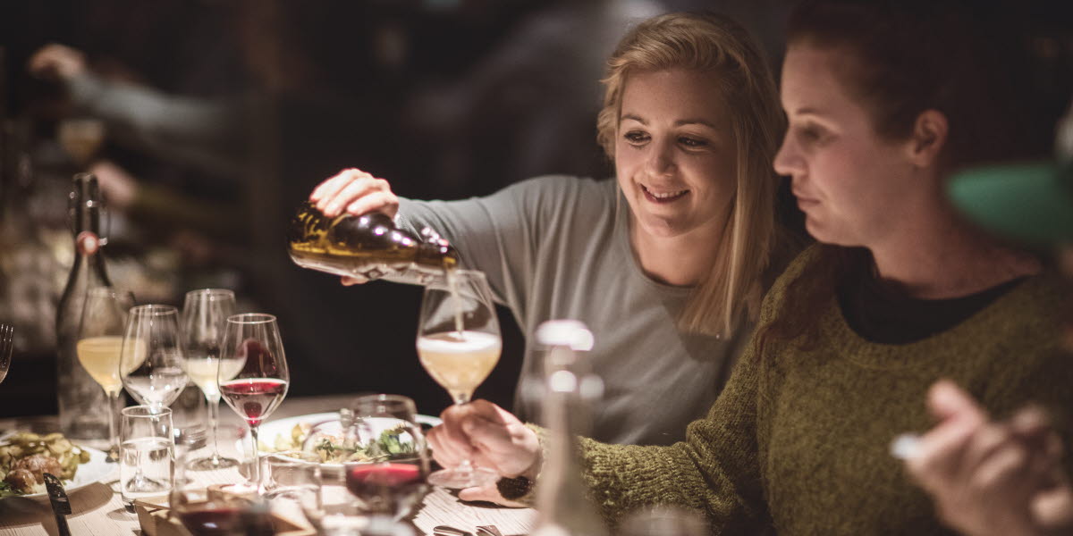 Kvinna fyller ett glas vid ett dukat bord