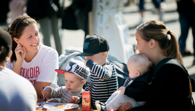 Two women and three children eating and talking at a table at a festival.