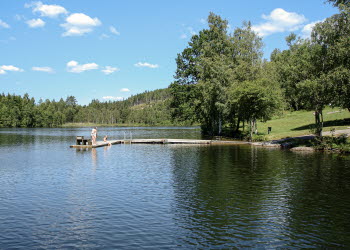 En bild på en stor sjö med en brygga. Runt om finns en grön och frodig växtlighet i form av gräsmatta och skog.