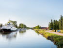 En stor vit passagerarbåt ligger vid Töreboda gästhamns brygg. Göta kanal syns och en promenadväg längs kanalen.