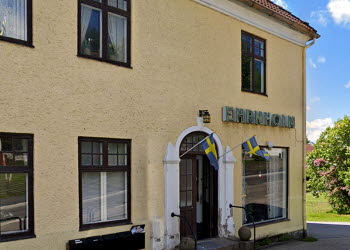 En bild på ett gult putsat hus med en vacker dörr som står öppen. På fasaden sitter en caféskylt.