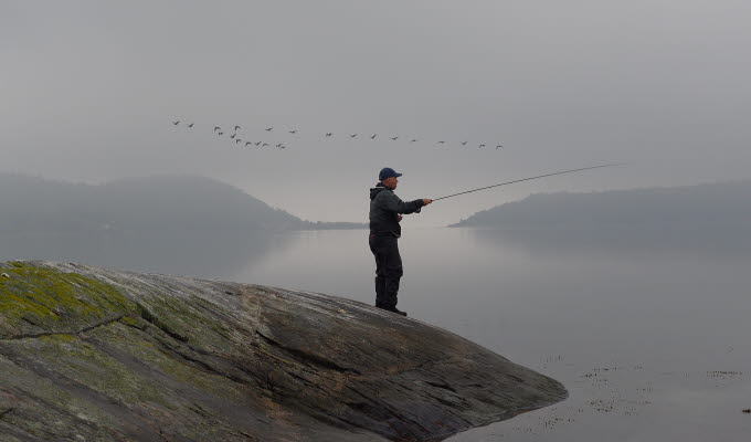 En man står på en klippa med sitt fiskespö.