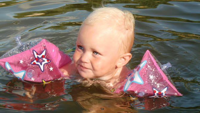 Liten flicka med rosa badpuffar badar i sjön.
